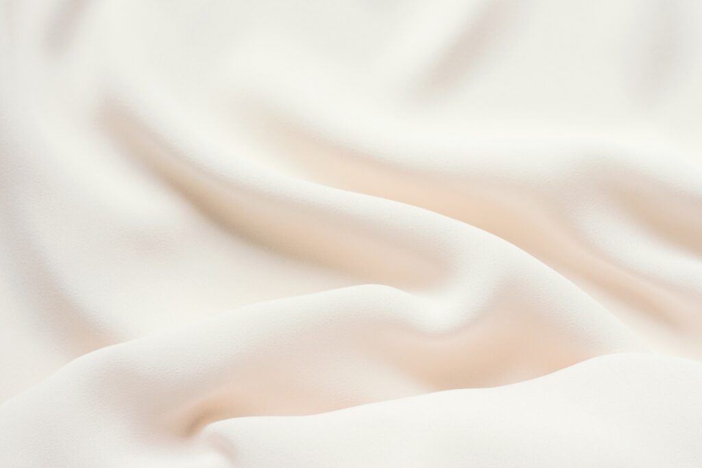 Matte cream delicate soft pleated fabric background. Smooth elegant luxury cloth texture. Gentle